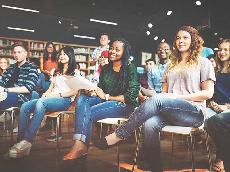 A diverse group of 10 people sit together during an event while watching a presenter that's not shown on the image.