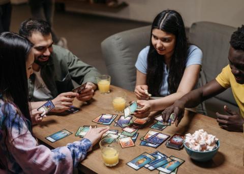 Four people sitting around a table playing a card game with drinks and snacks.