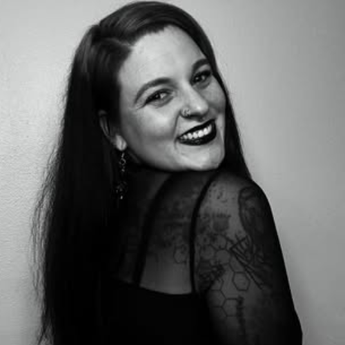 Person smiling over shoulder in black-and-white portrait, showing sheer patterned sleeve.