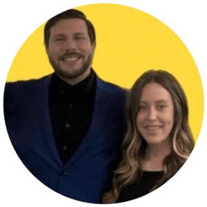 Two people smiling, standing close together against a solid yellow circular background.