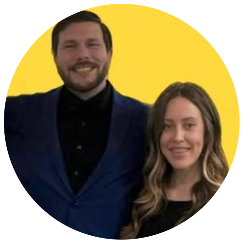 Two people smiling, standing close together against a solid yellow circular background.